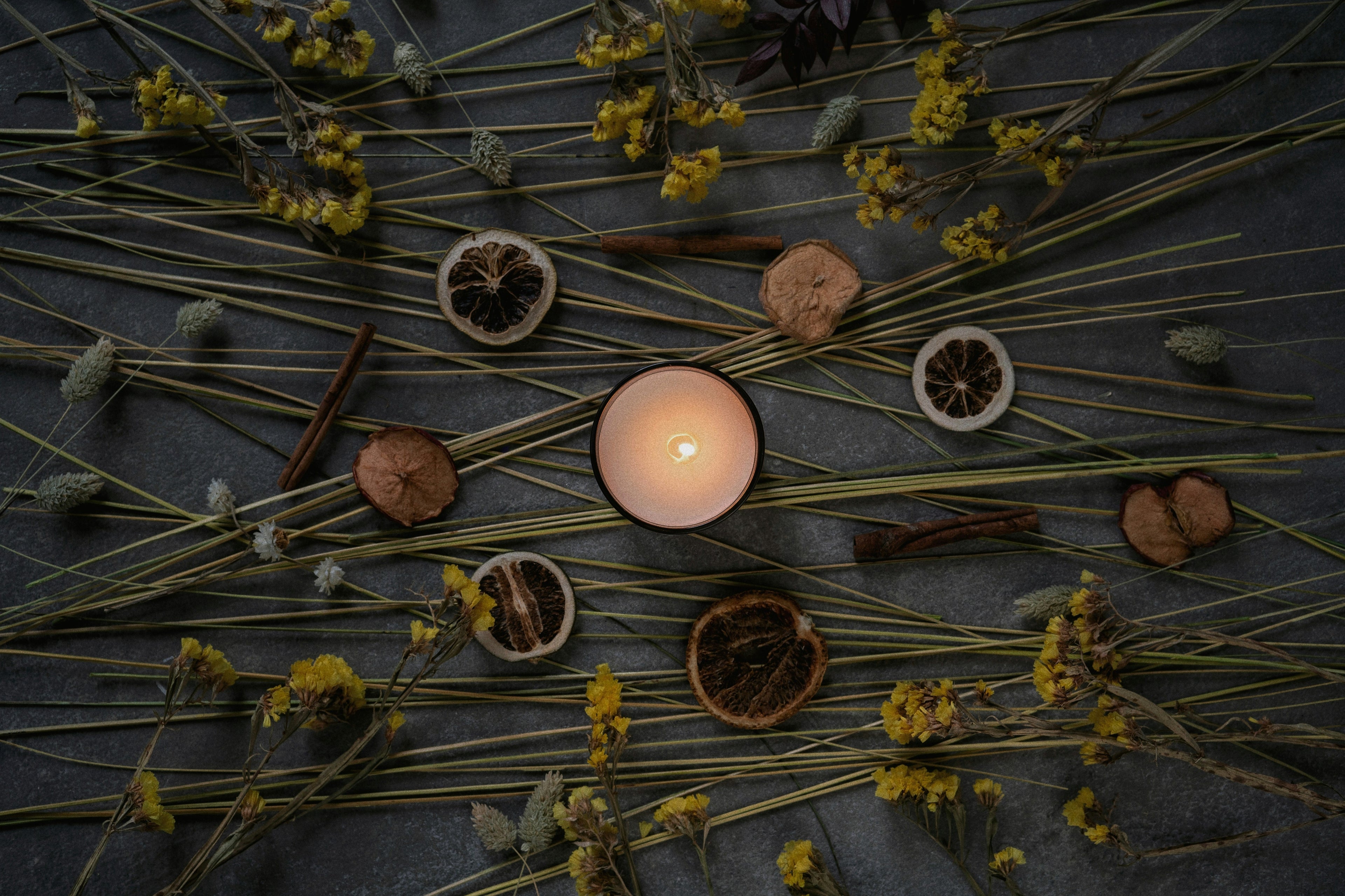 Candle surrounded by dried flowers and herbs on a dark surface